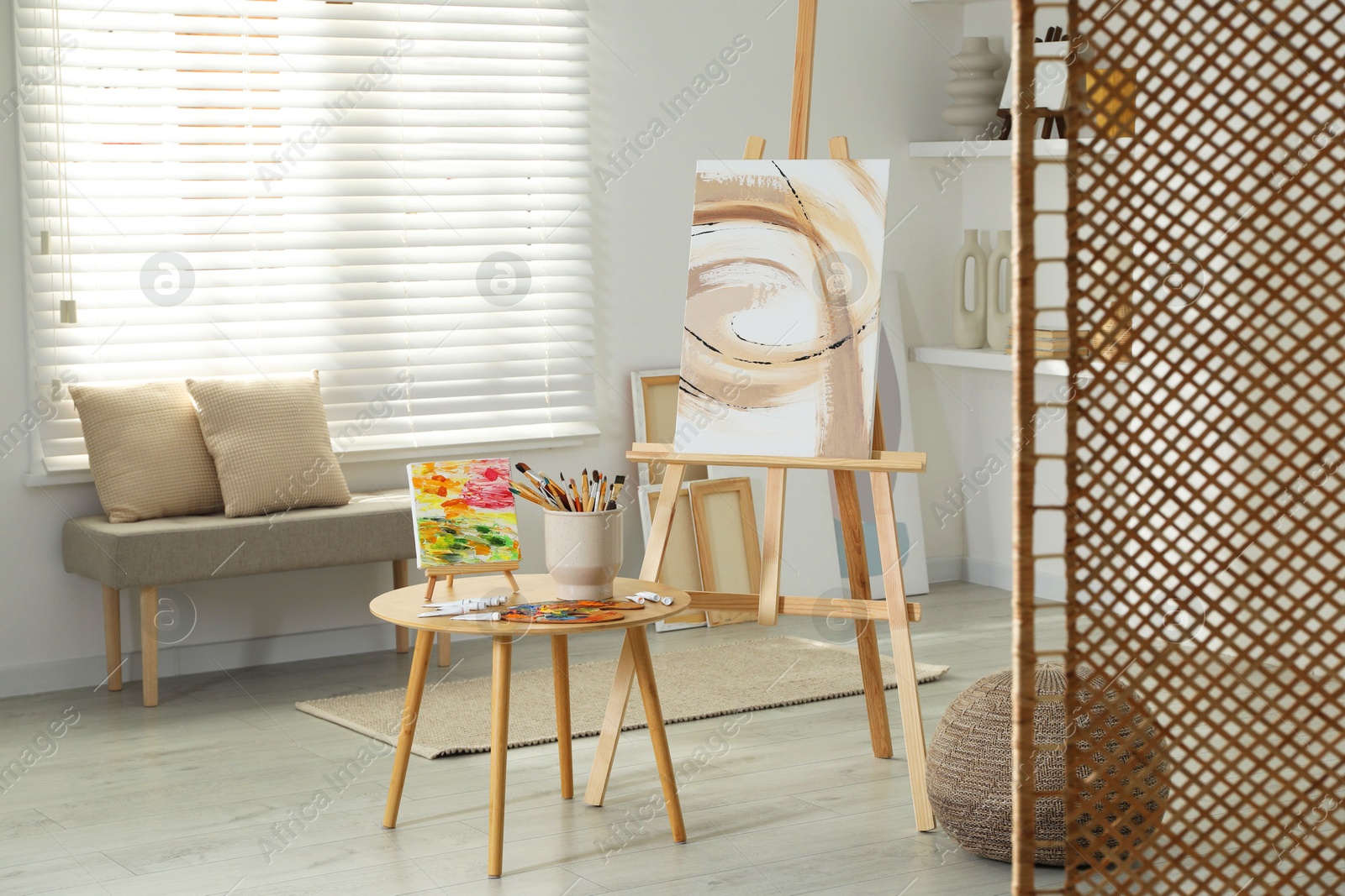 Photo of Folding screen and easels with beautiful abstract paintings in room