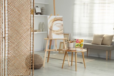 Photo of Folding screen and easels with beautiful abstract paintings in room