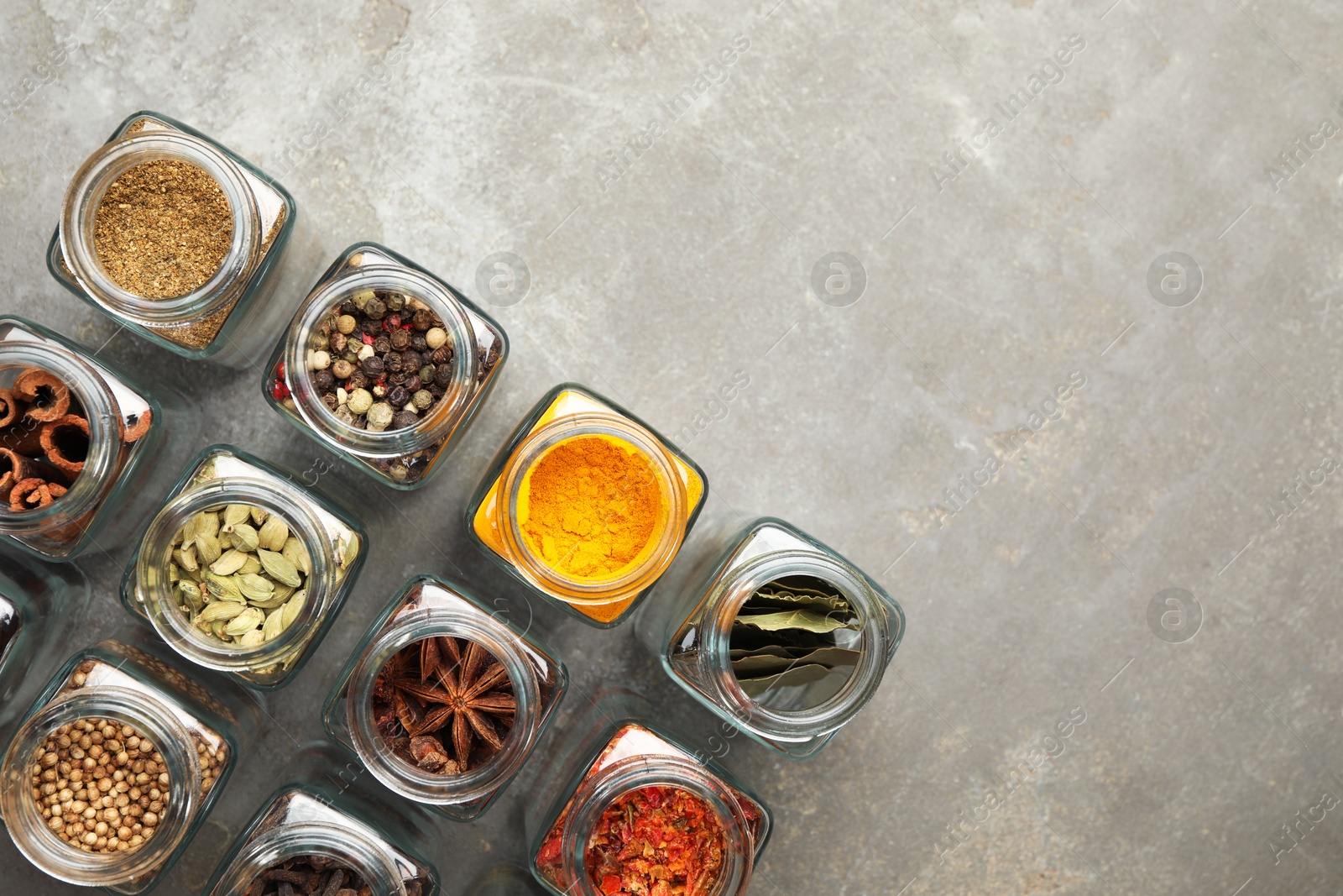 Photo of Different spices in glass jars on grey table, flat lay. Space for text