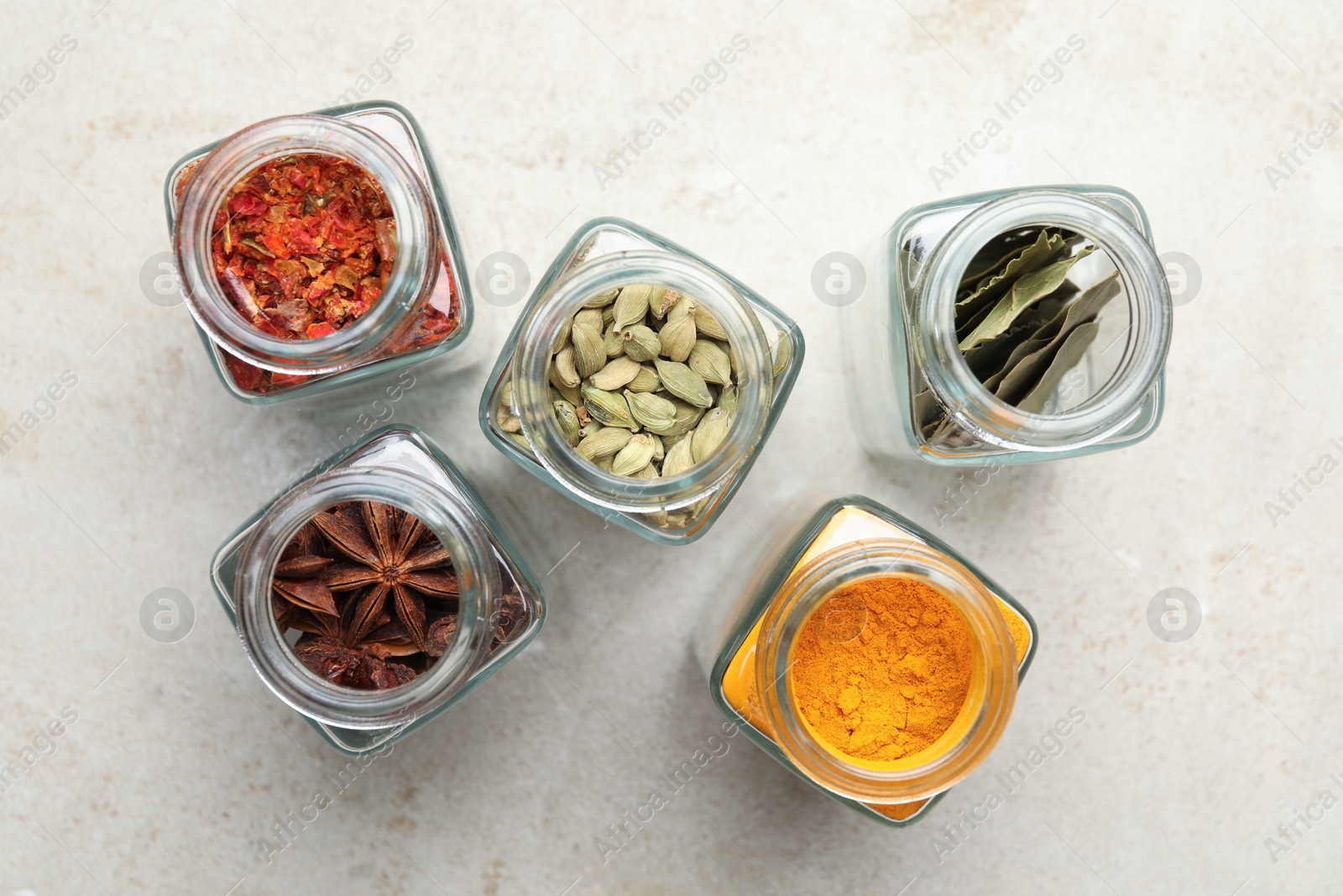 Photo of Different spices in glass jars on light grey table, flat lay