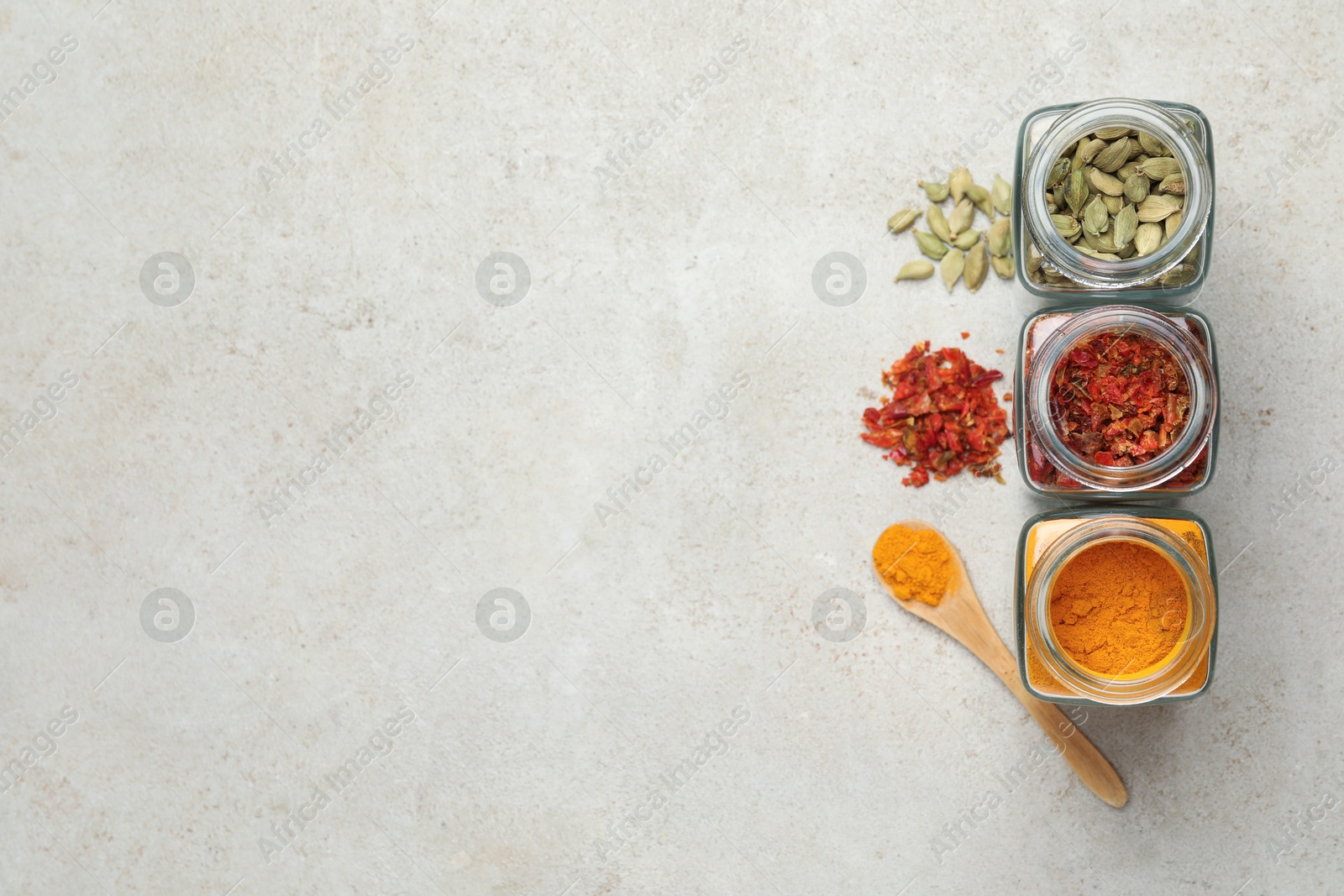 Photo of Different spices in glass jars on light grey table, flat lay. Space for text