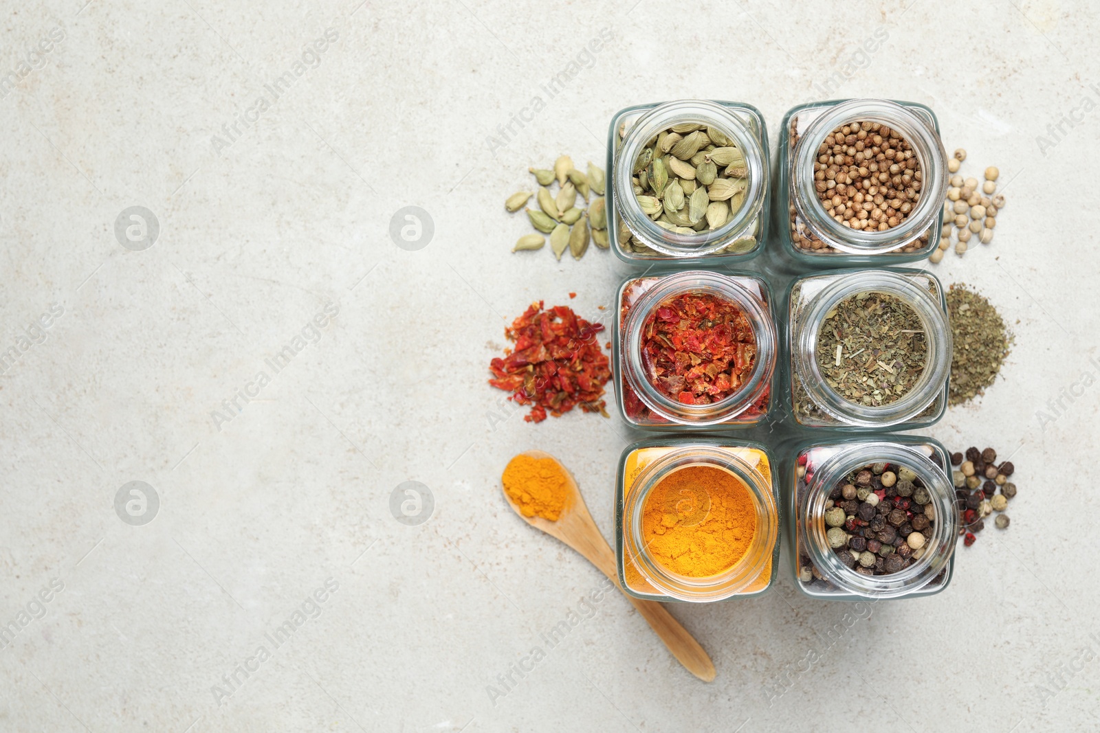 Photo of Different spices in glass jars on light grey table, top view. Space for text