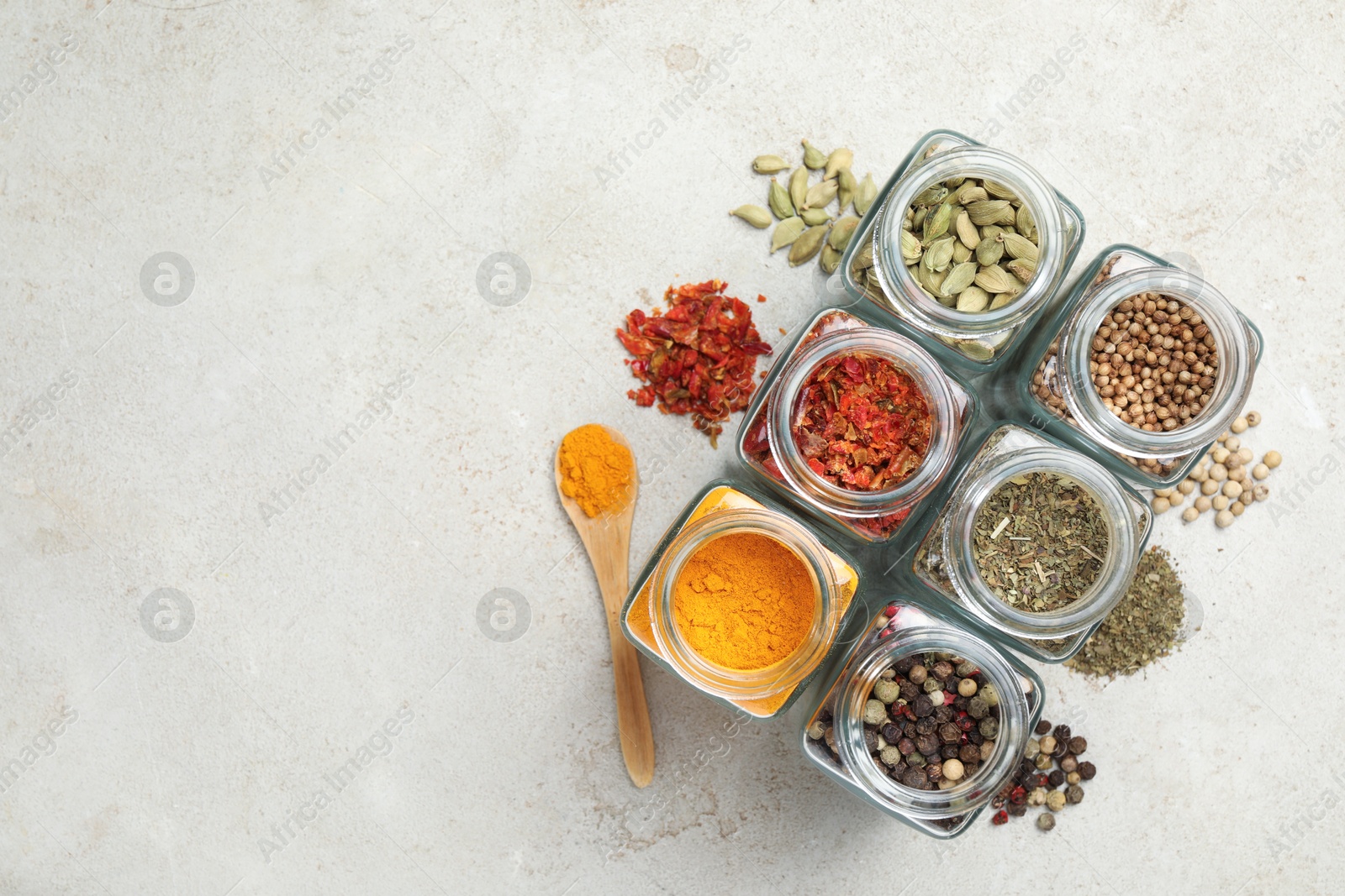 Photo of Different spices in glass jars on light grey table, top view. Space for text