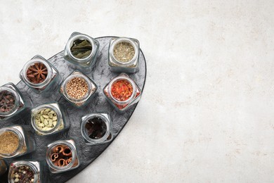 Photo of Different spices in glass jars on light grey table, top view. Space for text