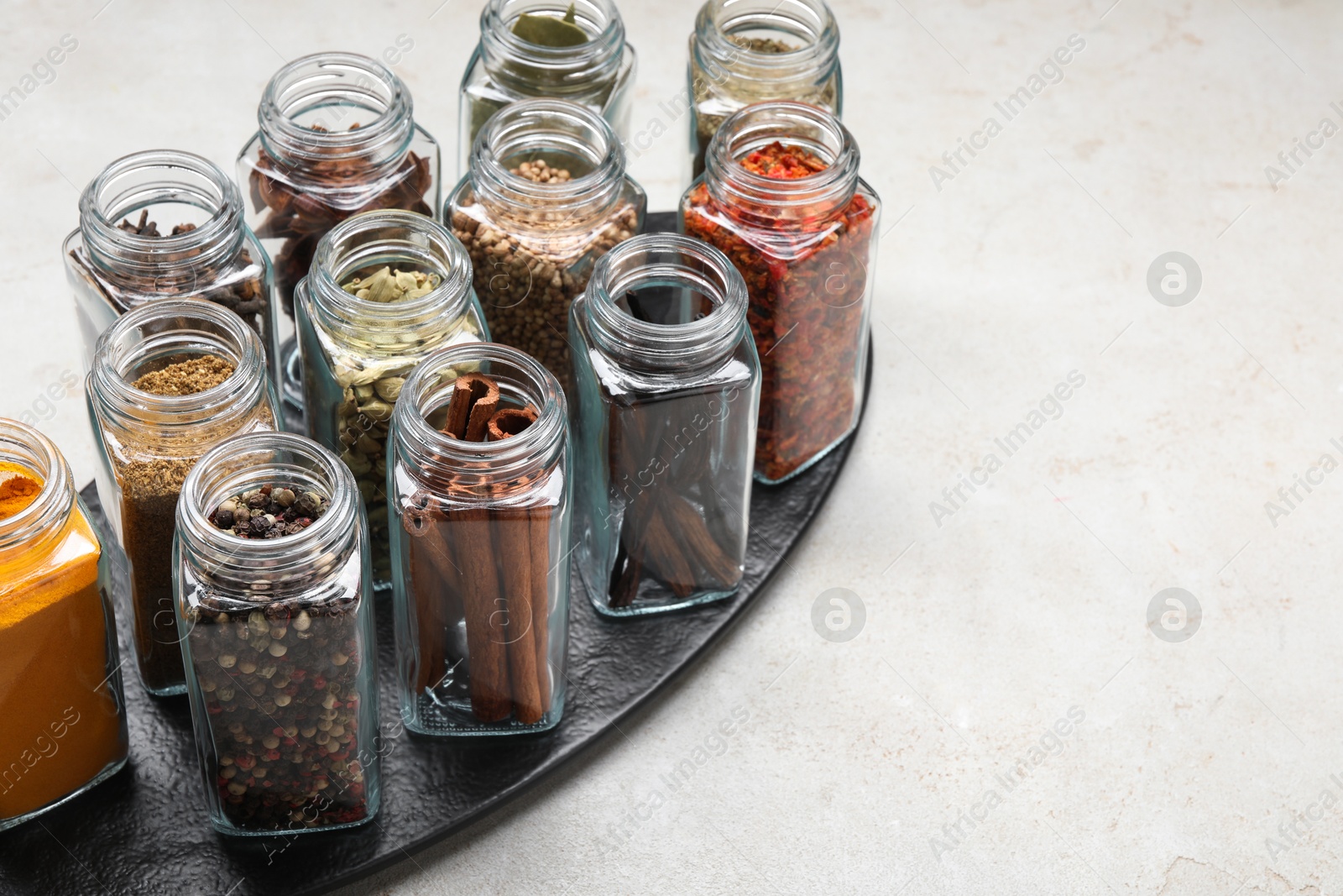 Photo of Different spices in glass jars on light grey table, space for text