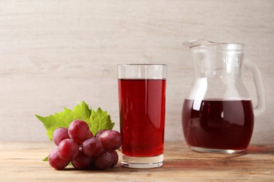 Tasty juice in glass, jug, fresh grapes and leaf on wooden table