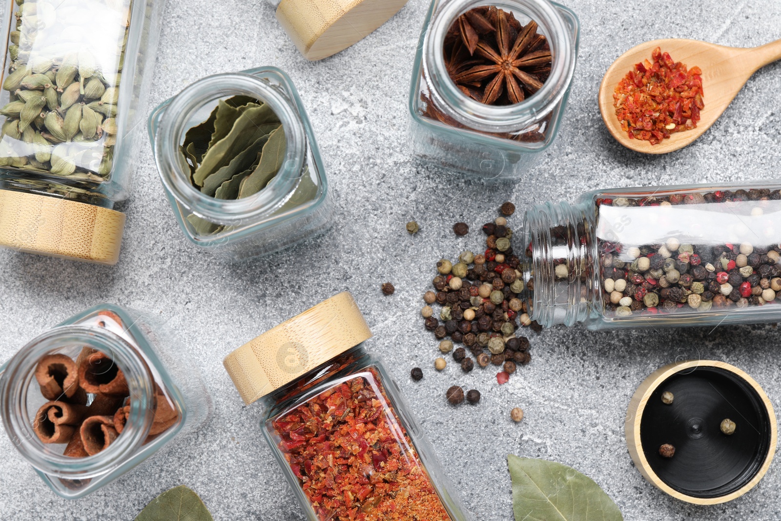 Photo of Different spices in glass jars on grey table, flat lay