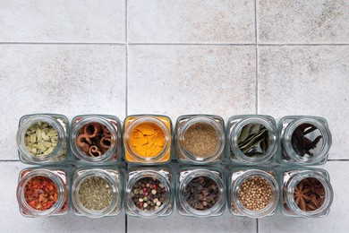 Photo of Different spices in glass jars on light tiled table, top view. Space for text