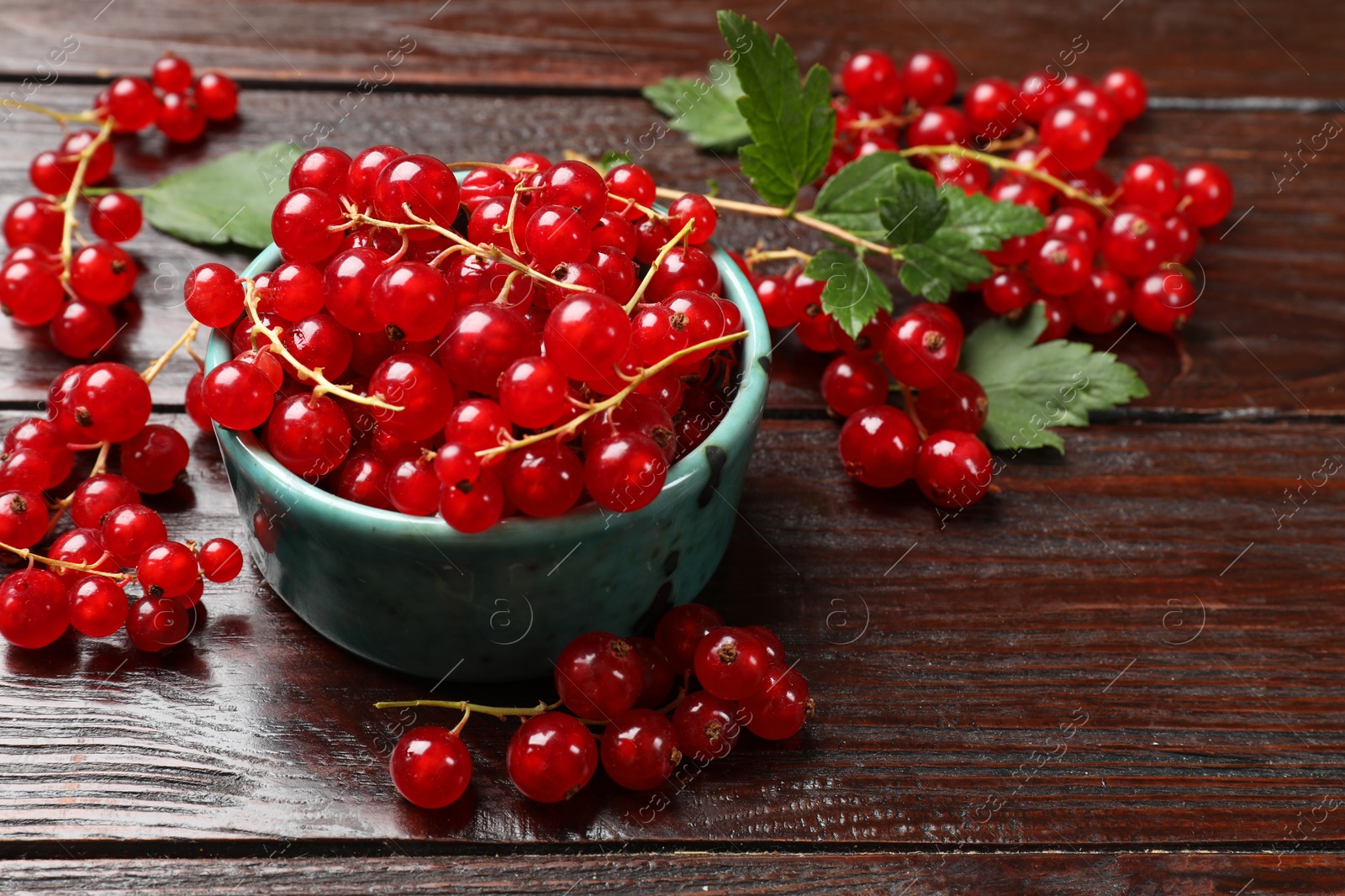 Photo of Fresh red currants and green leaves on wooden table, closeup