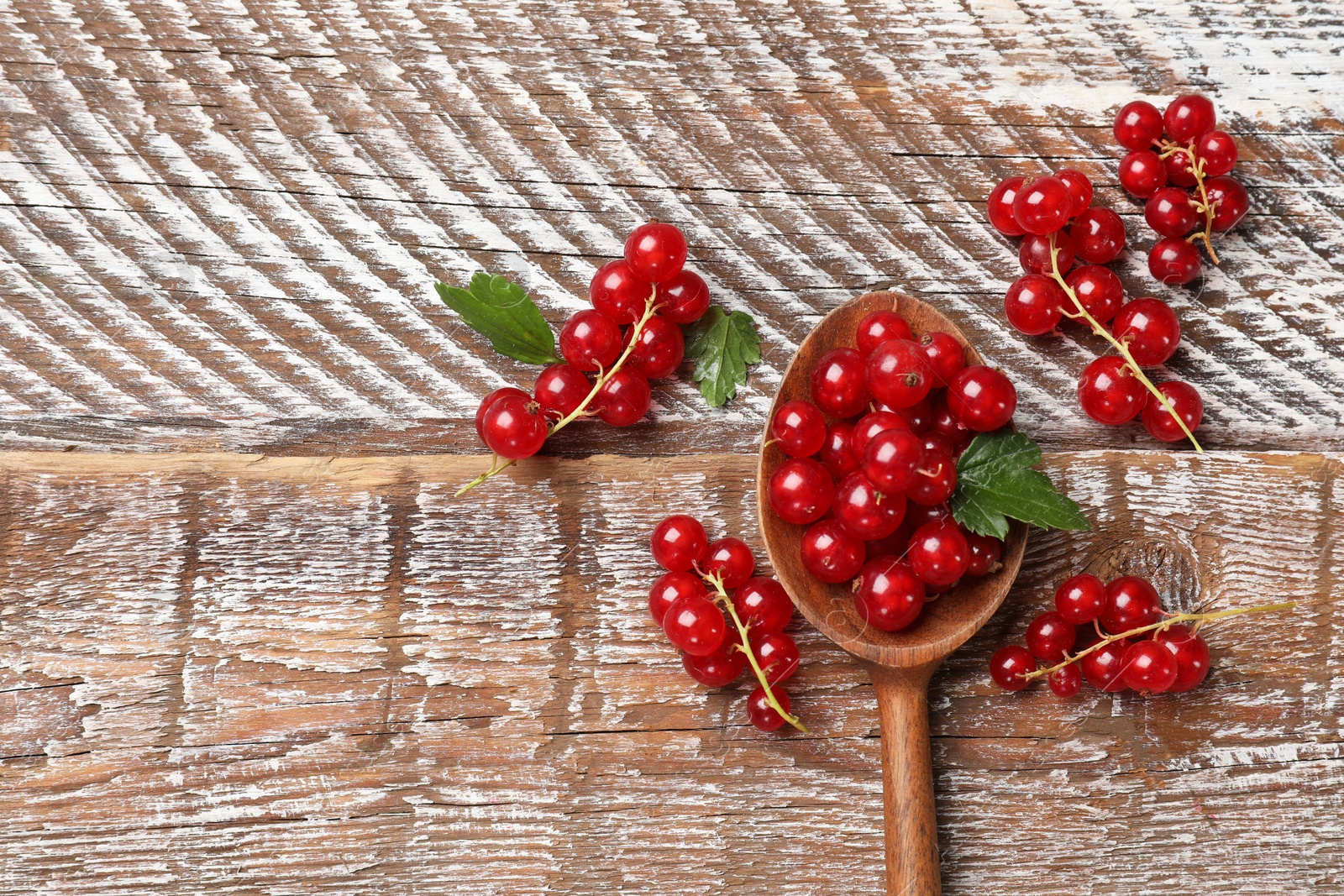 Photo of Fresh red currants and green leaves on wooden table, top view. Space for text