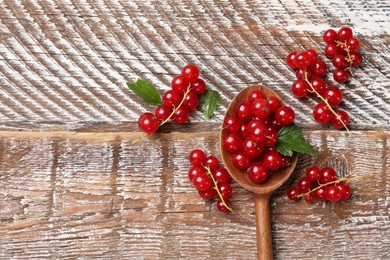 Photo of Fresh red currants and green leaves on wooden table, top view. Space for text