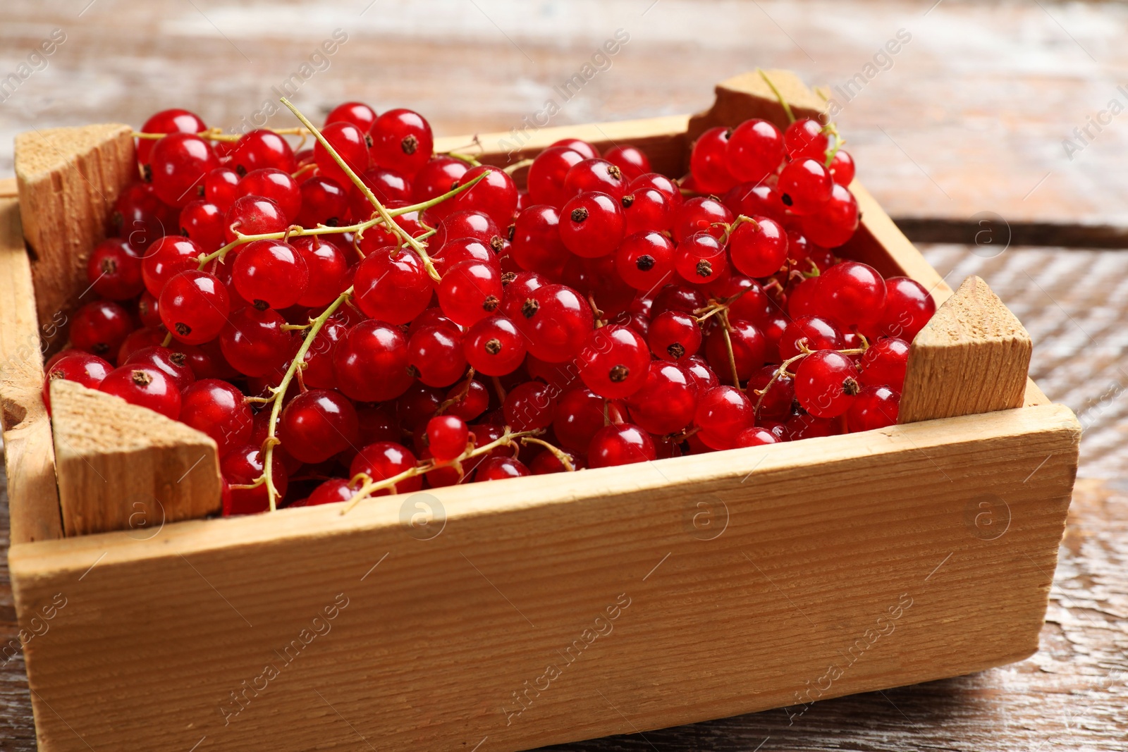 Photo of Fresh red currants in crate on wooden table, closeup