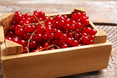 Photo of Fresh red currants in crate on wooden table, closeup