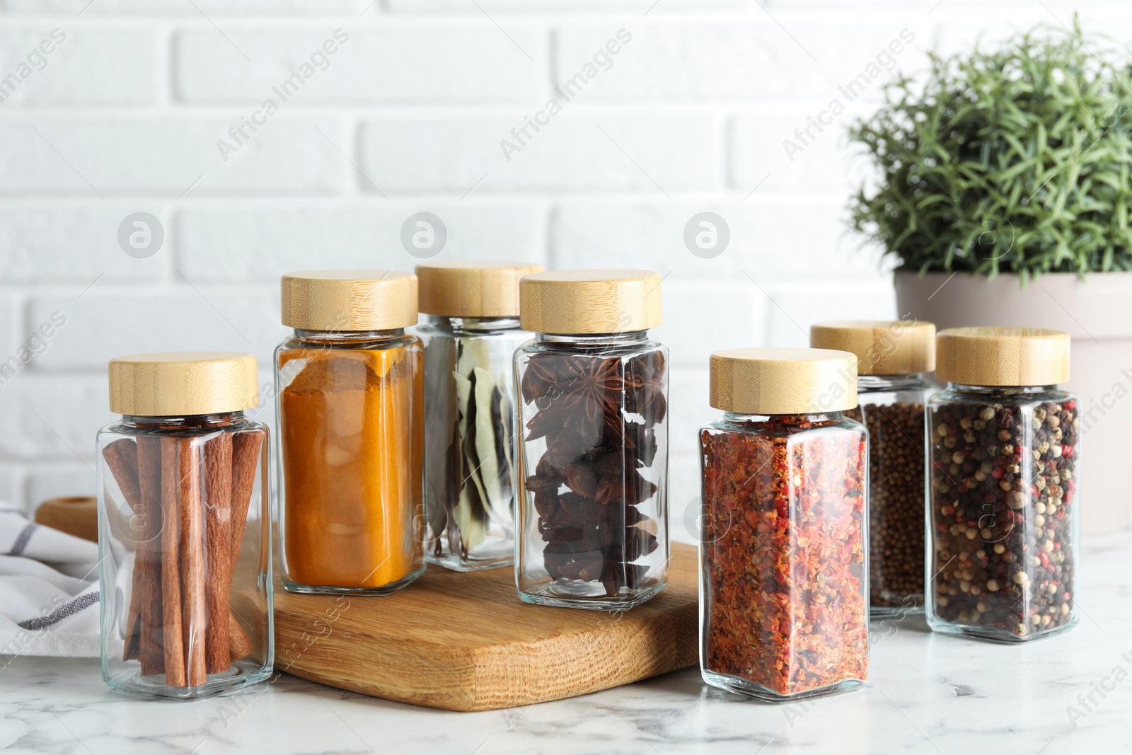 Photo of Different spices in glass jars on white marble table