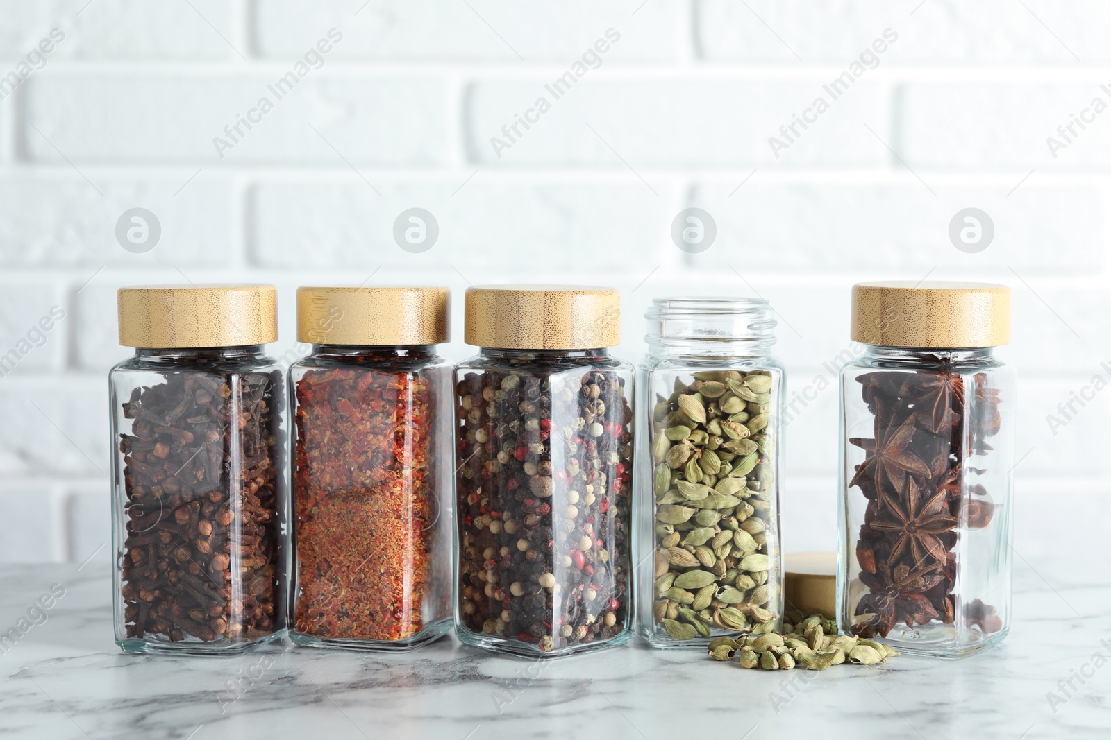 Photo of Different spices in glass jars on white marble table