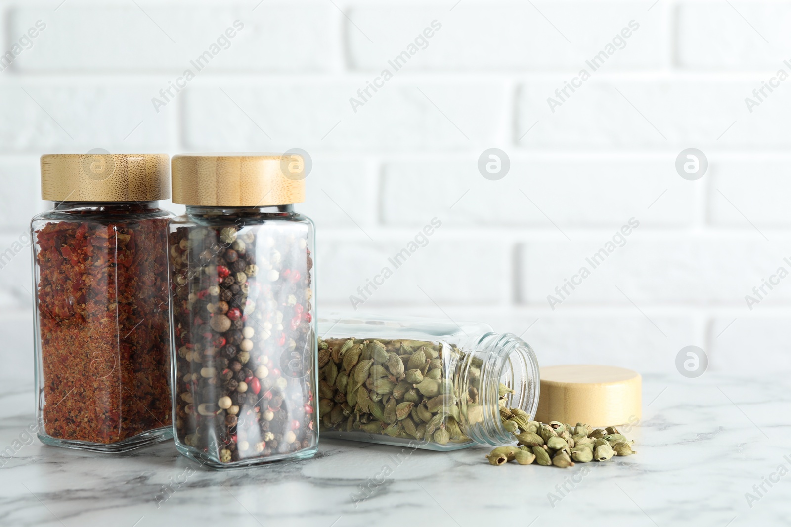 Photo of Different spices in glass jars on white marble table