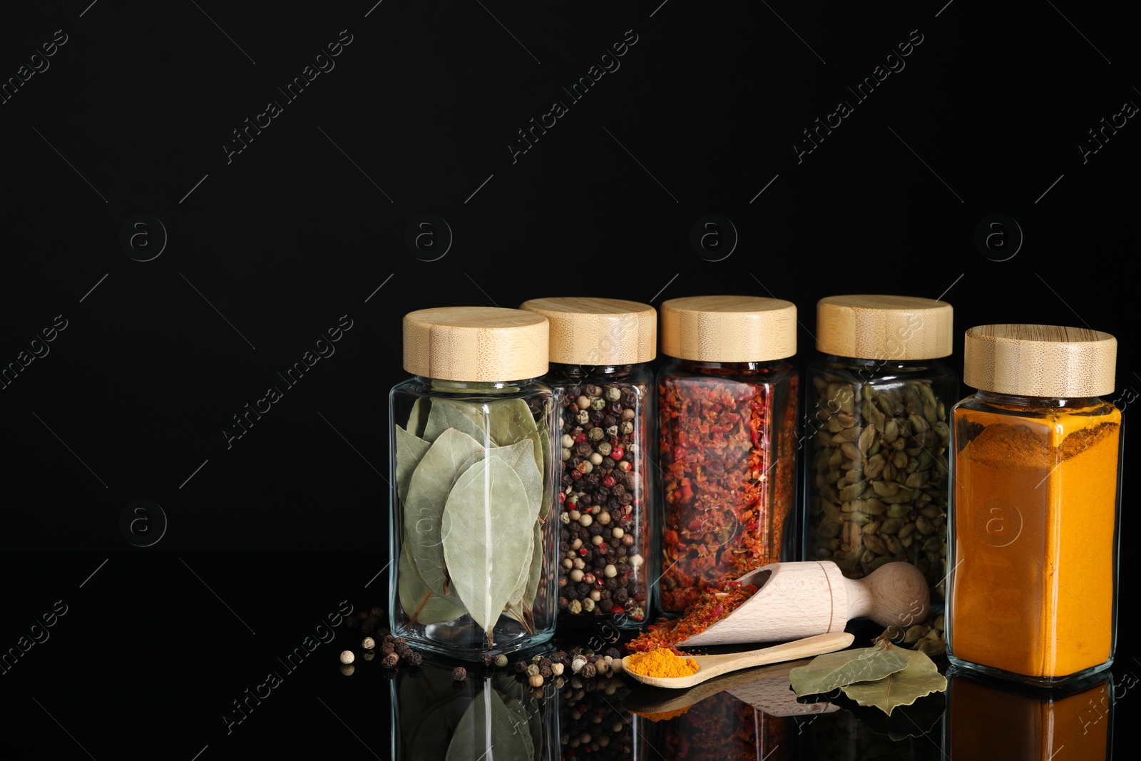 Photo of Different spices in glass jars on black mirror surface, space for text