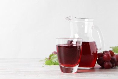 Photo of Tasty grape juice, leaves and berries on light wooden table. Space for text