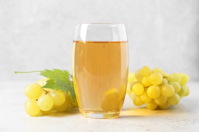 Tasty grape juice in glass, leaf and berries on light textured table, closeup