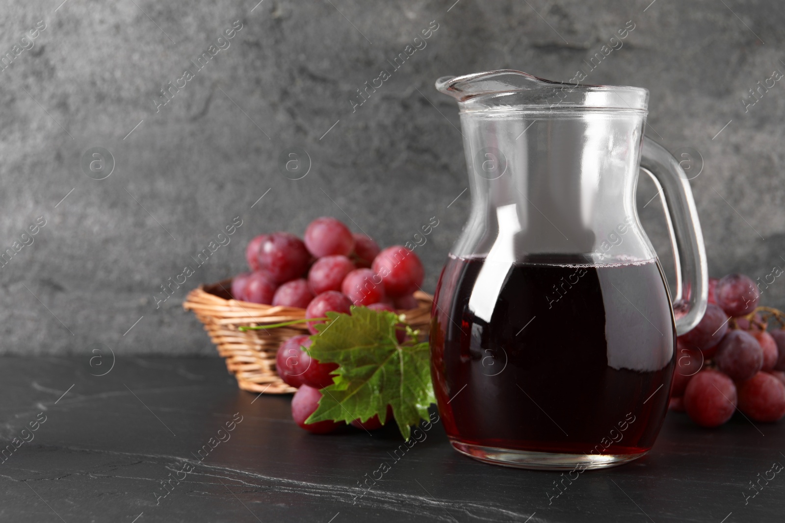 Photo of Tasty grape juice in jar, leaf and berries on dark textured table, closeup. Space for text