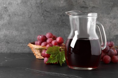 Photo of Tasty grape juice in jar, leaf and berries on dark textured table, closeup. Space for text