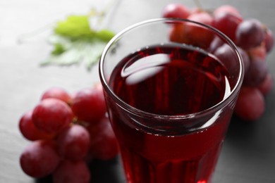 Photo of Tasty grape juice in glass and berries on table, closeup