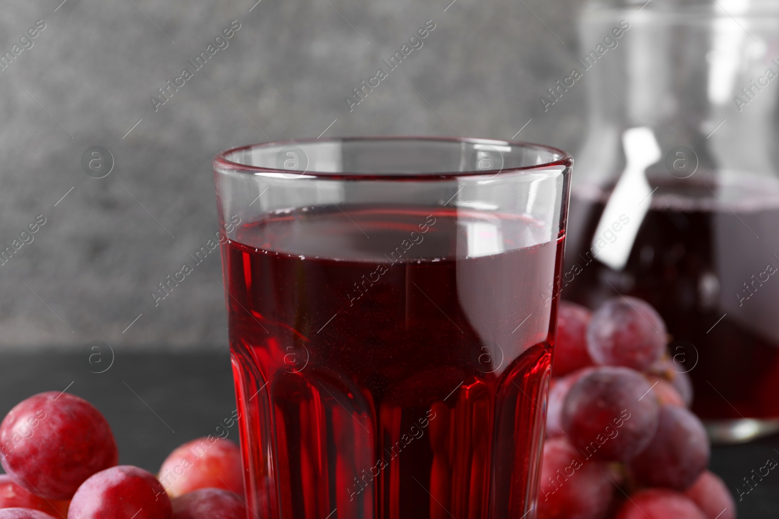 Photo of Tasty grape juice in glass and berries on table, closeup