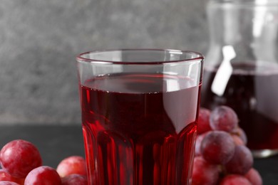 Photo of Tasty grape juice in glass and berries on table, closeup