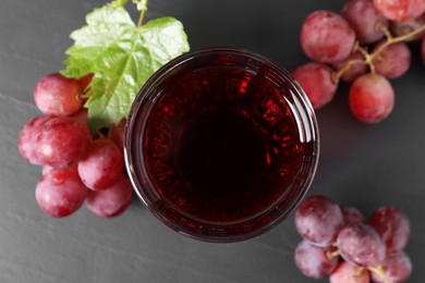 Tasty grape juice in glass, leaf and berries on dark textured table, flat lay