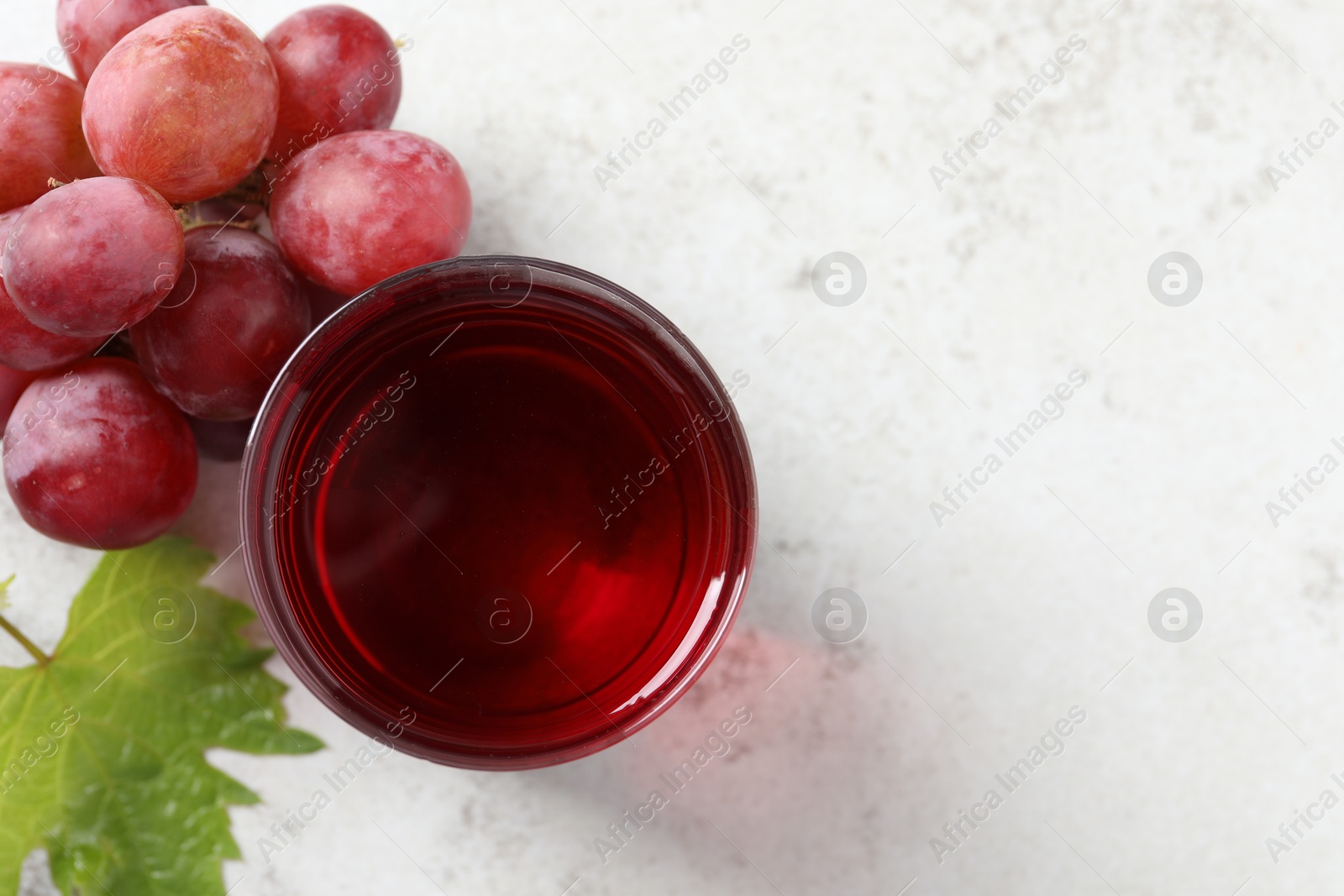 Photo of Tasty grape juice in glass, leaf and berries on light table, flat lay. Space for text