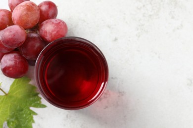 Tasty grape juice in glass, leaf and berries on light table, flat lay. Space for text