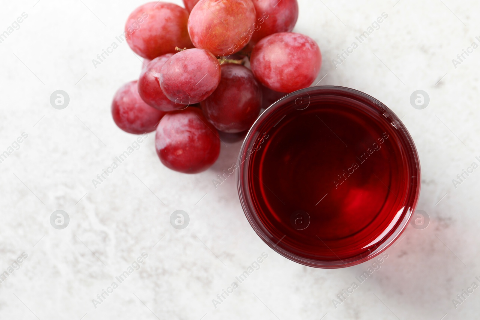 Photo of Tasty grape juice in glass and berries on light table, flat lay. Space for text