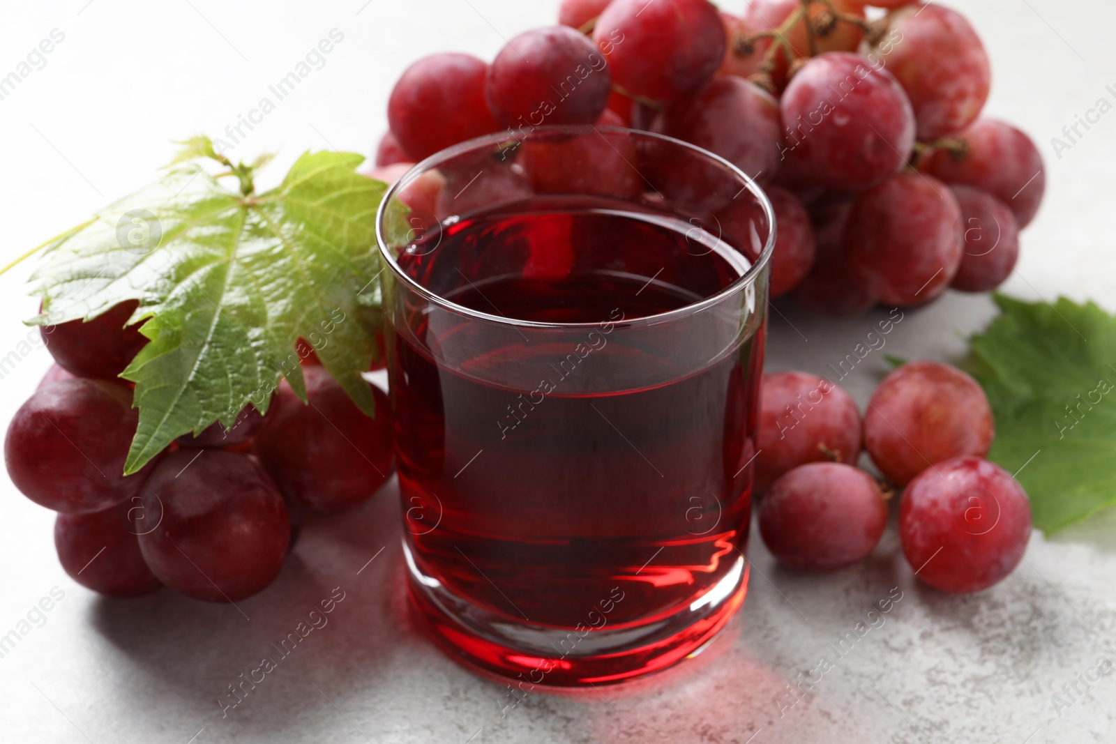 Photo of Tasty grape juice in glass, leaves and berries on light textured table, closeup