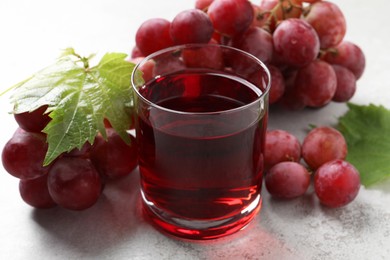 Tasty grape juice in glass, leaves and berries on light textured table, closeup