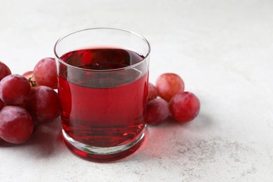 Photo of Tasty grape juice in glass and berries on light textured table, closeup. Space for text