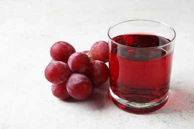 Photo of Tasty grape juice in glass and berries on light textured table, closeup