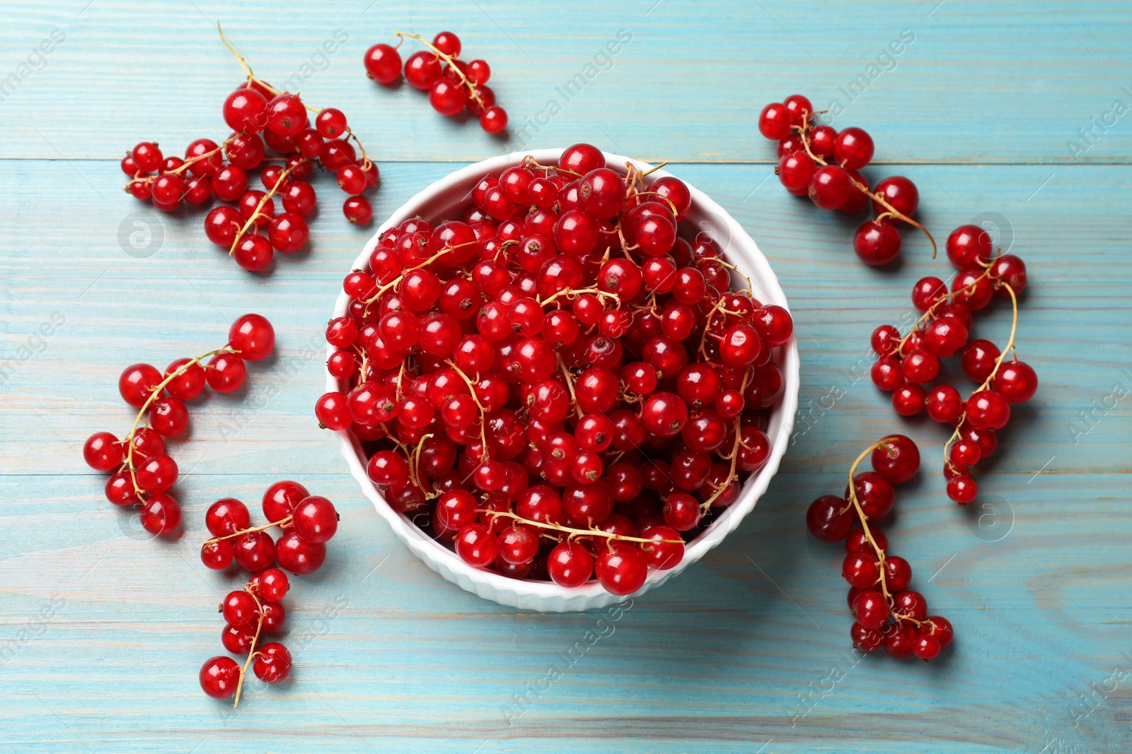 Photo of Fresh red currants in bowl on light blue wooden table, top view