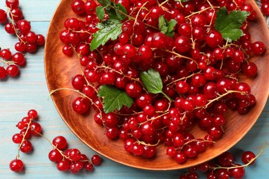 Fresh red currants and leaves on light blue wooden table, flat lay