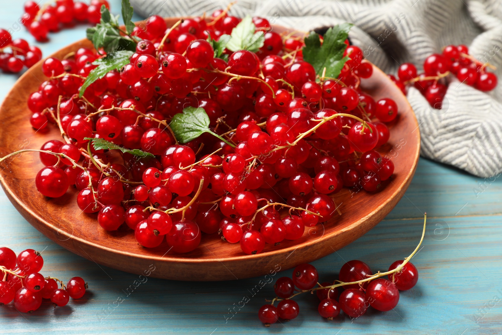 Photo of Fresh red currants and leaves on light blue wooden table, closeup