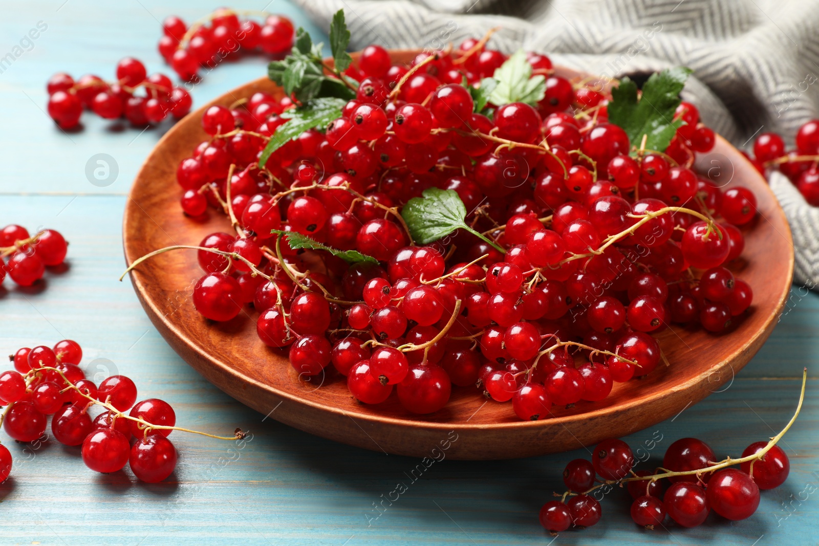 Photo of Fresh red currants and leaves on light blue wooden table, closeup