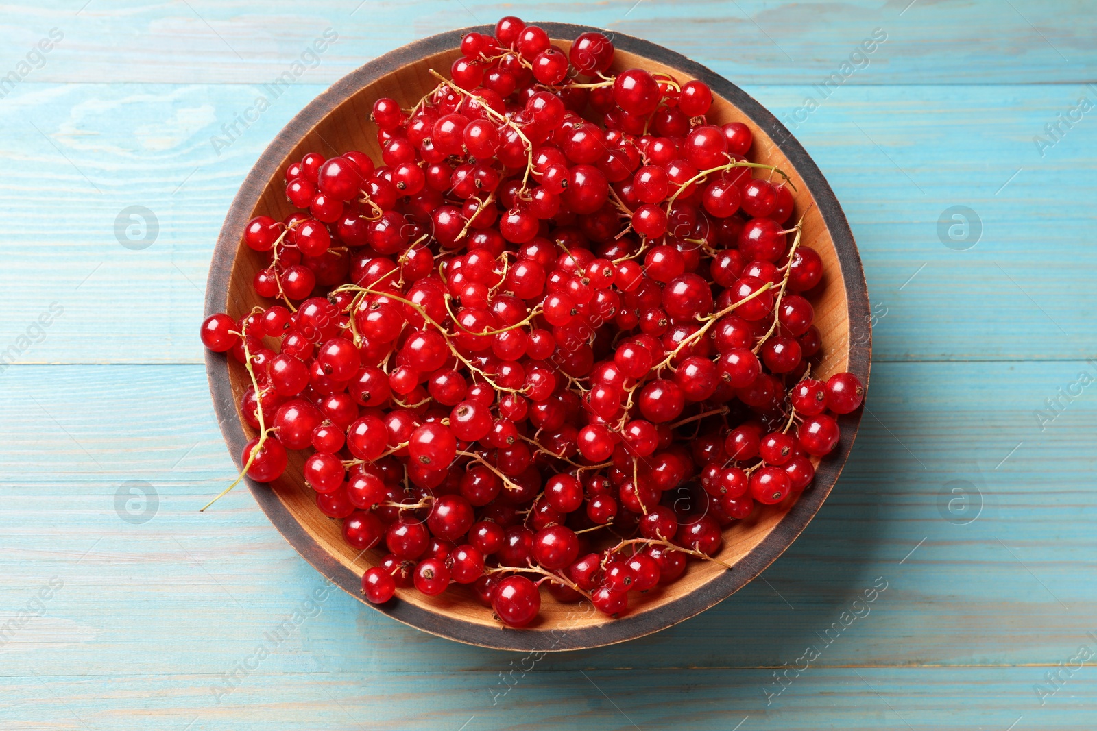 Photo of Fresh red currants in bowl on light blue wooden table, top view