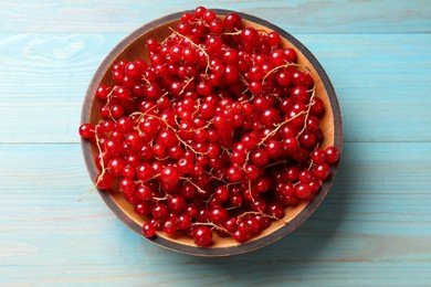 Fresh red currants in bowl on light blue wooden table, top view