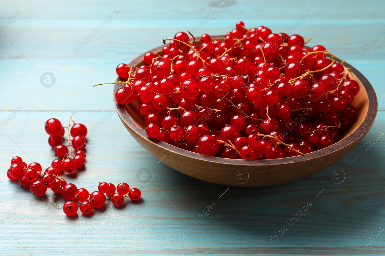 Photo of Fresh red currants in bowl on light blue wooden table, closeup