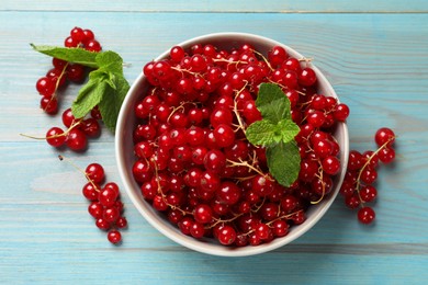 Fresh red currants in bowl and mint on light blue wooden table, top view