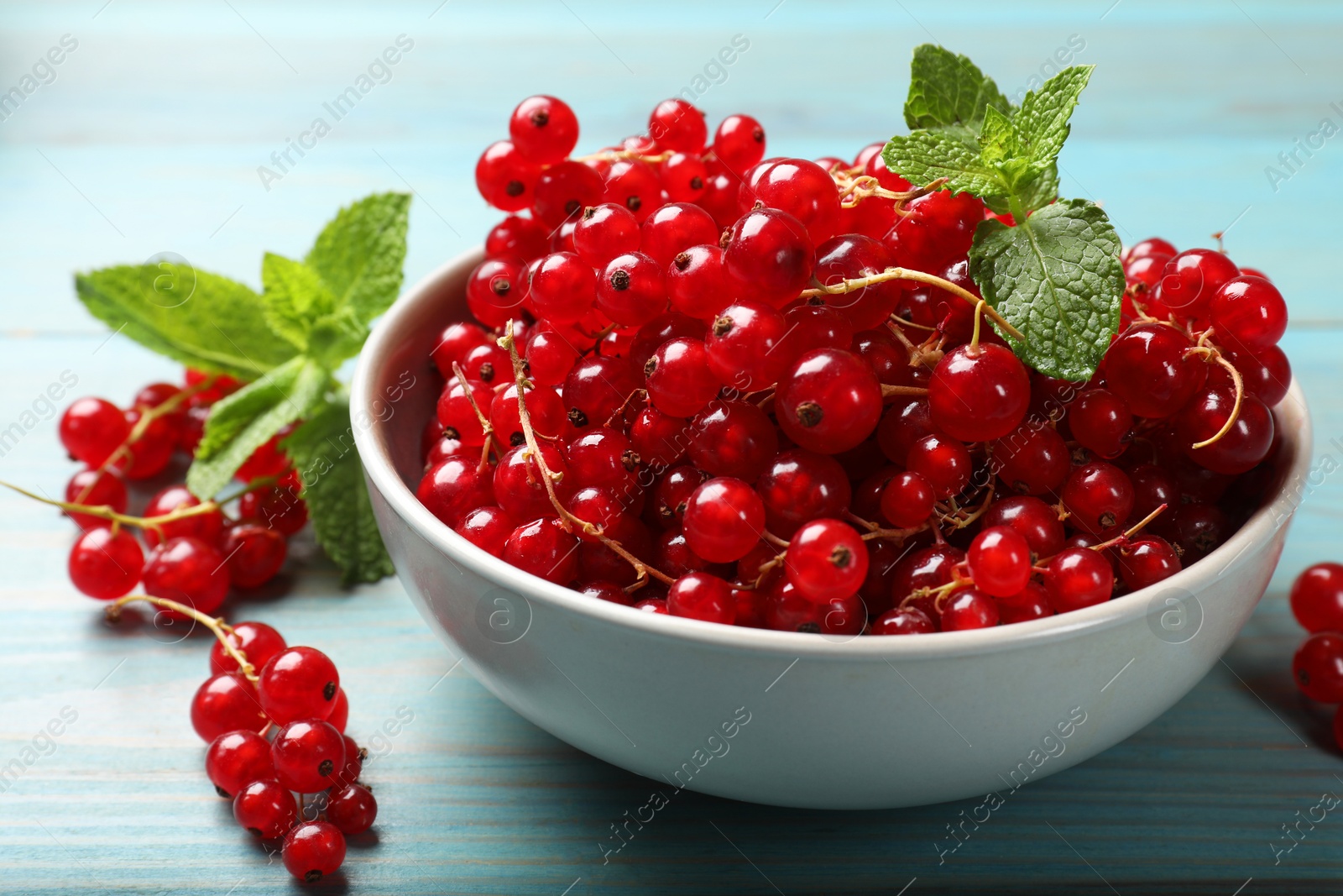 Photo of Fresh red currants in bowl and mint on light blue wooden table, closeup