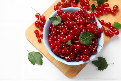 Photo of Fresh red currants in bowl and green leaves on white table, top view