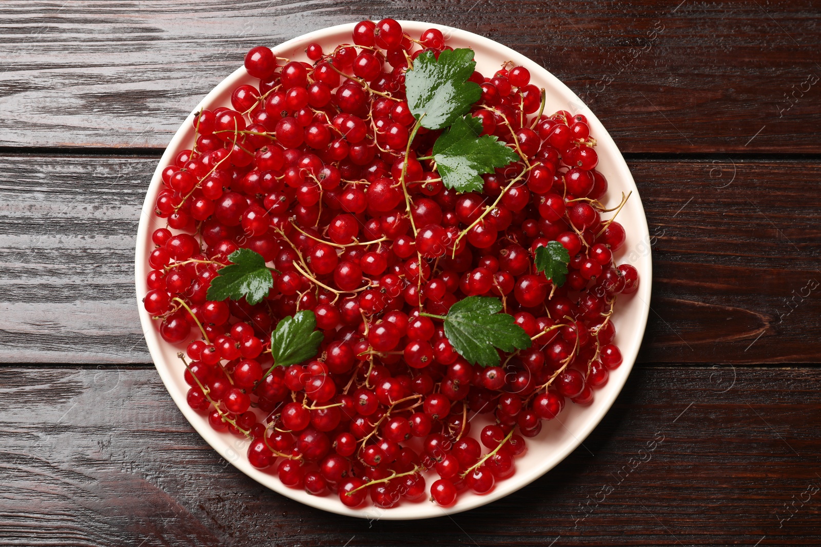 Photo of Fresh red currants and green leaves on wooden table, top view