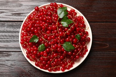 Photo of Fresh red currants and green leaves on wooden table, top view