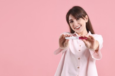 Happy young woman with pregnancy test on pink background, space for text