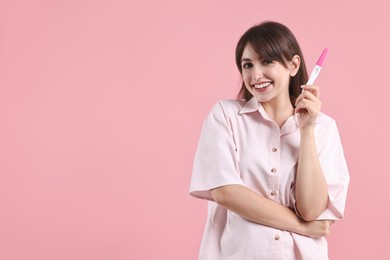 Happy young woman with pregnancy test on pink background, space for text